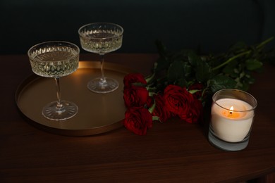 Photo of Burning candle, glasses of wine and beautiful red roses on wooden table indoors