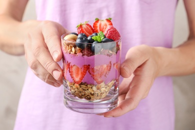 Woman holding glass of acai dessert with granola and berries, closeup