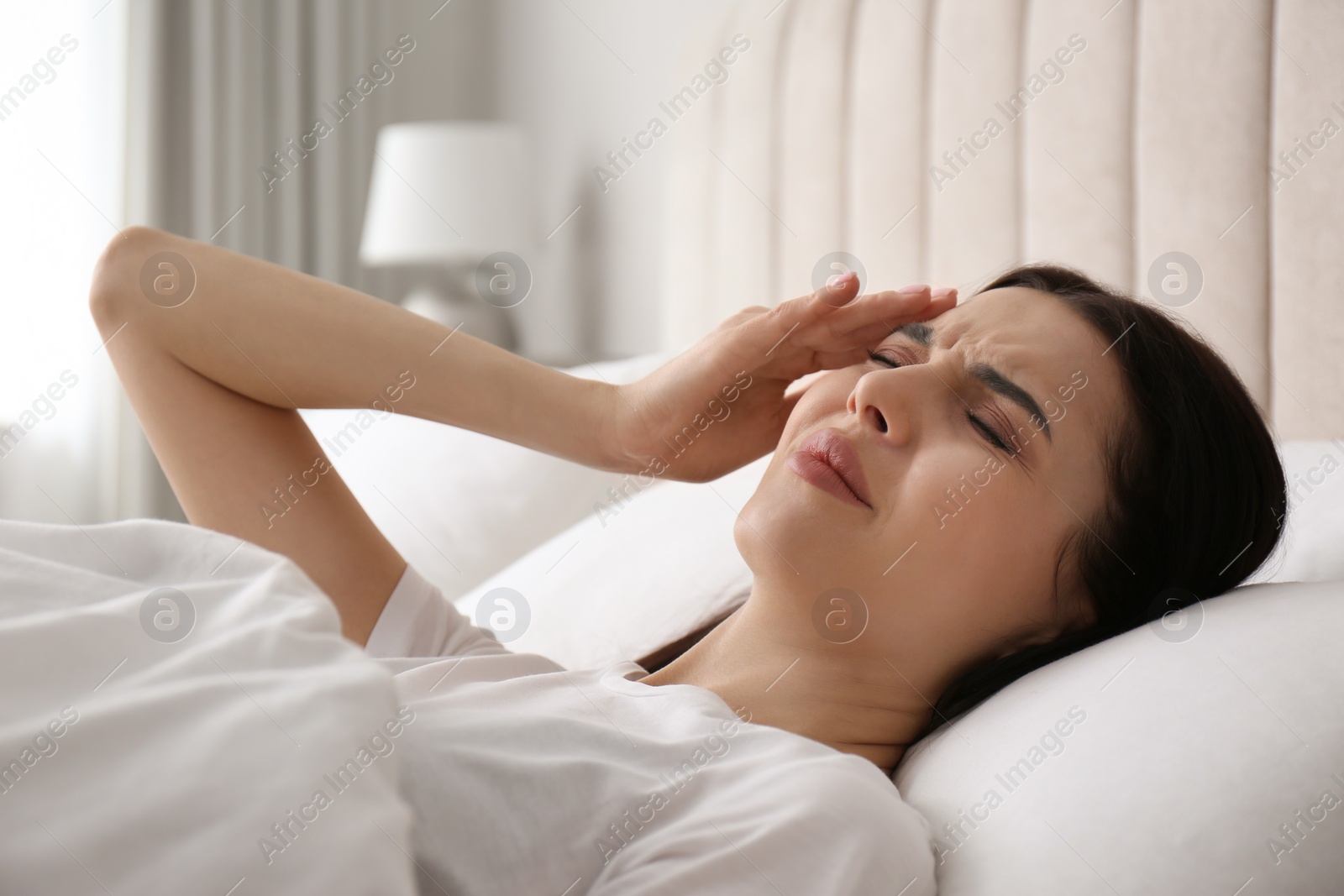 Photo of Young woman suffering from migraine in bed at home