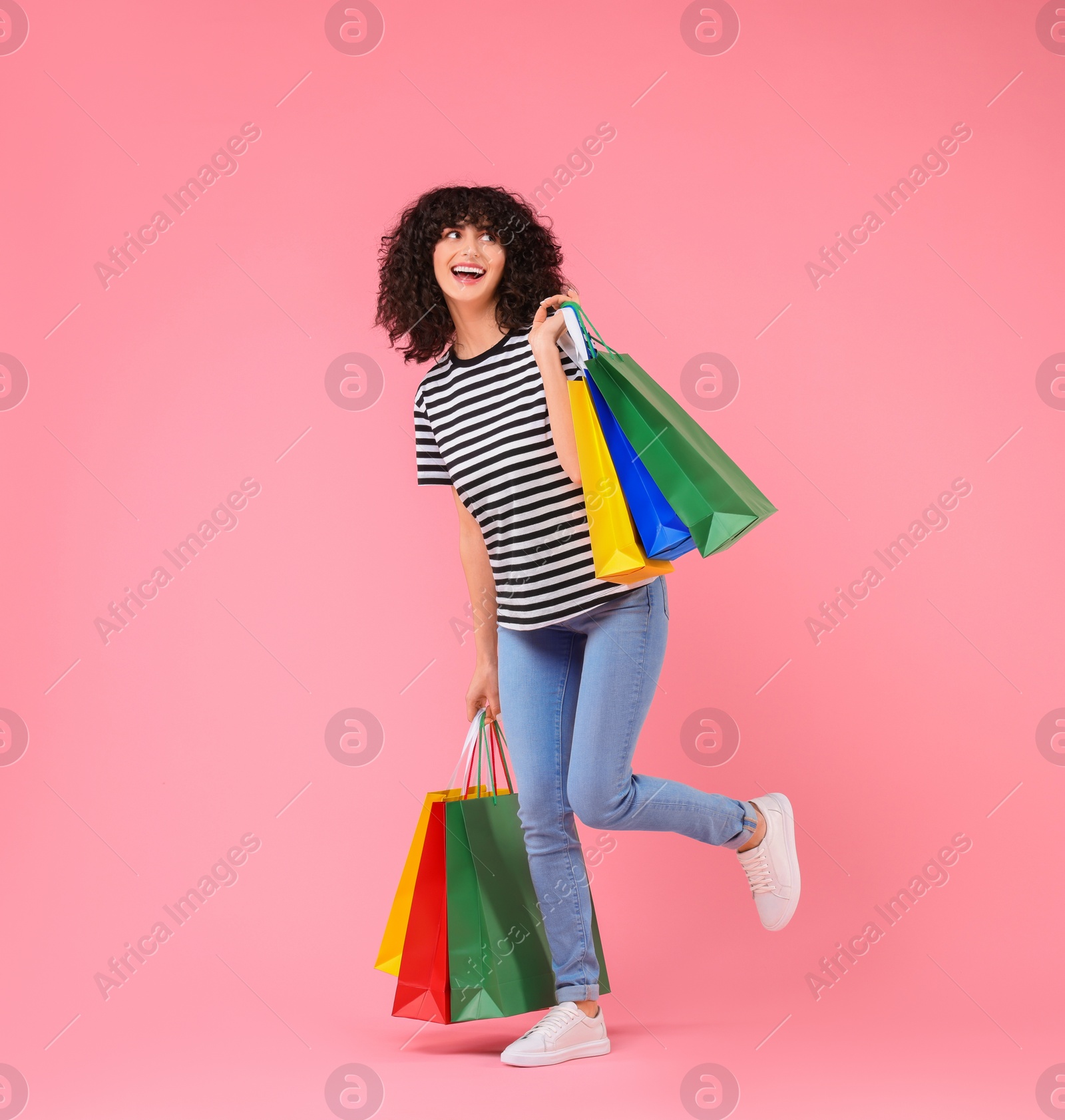 Photo of Happy young woman with shopping bags on pink background