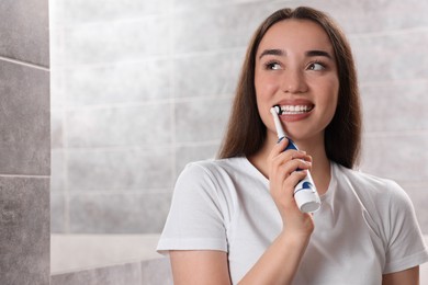 Young woman brushing her teeth with electric toothbrush in bathroom