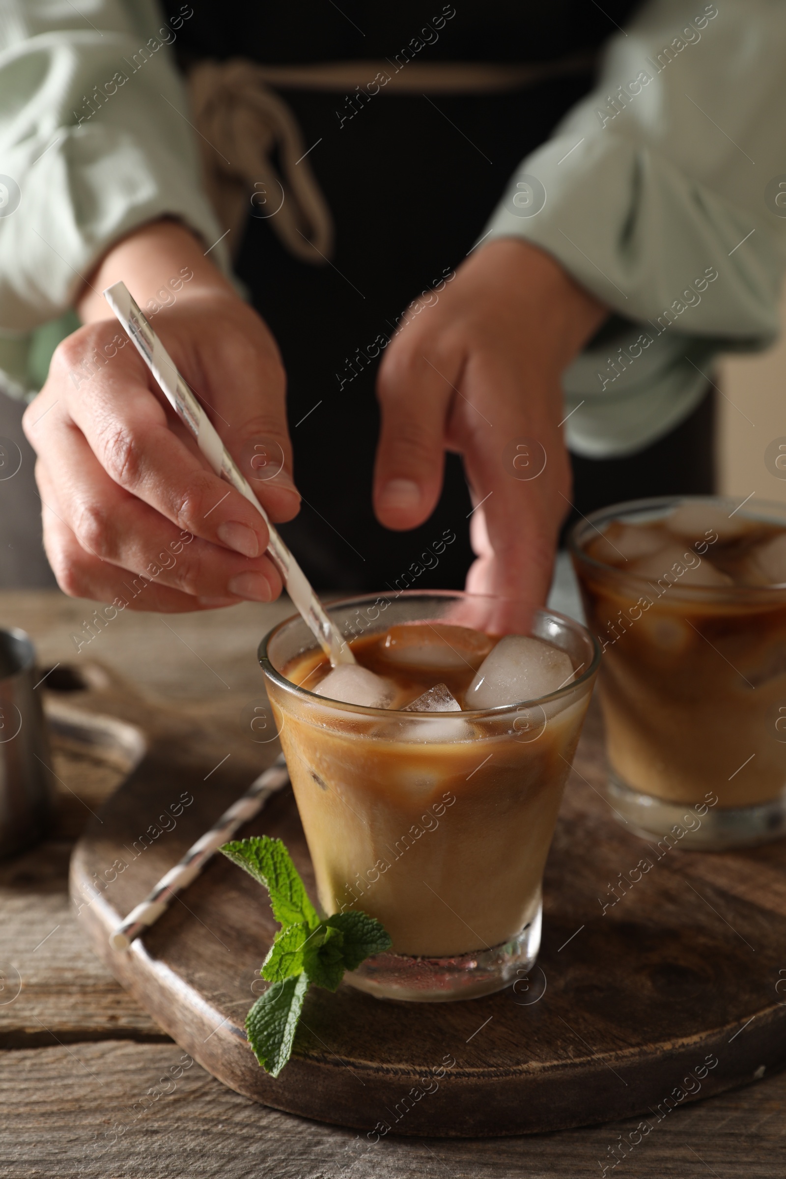 Photo of Woman stirring iced coffee with straw at wooden table, closeup