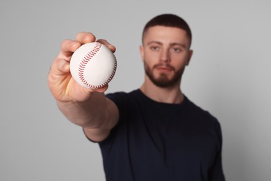 Photo of Athletic young man with baseball ball on light grey background, selective focus