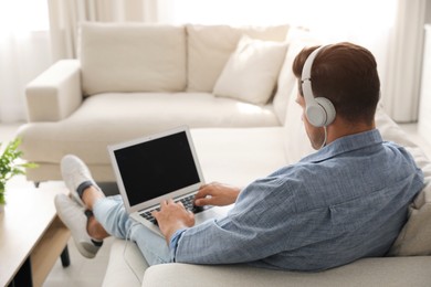 Man with laptop and headphones sitting on sofa at home