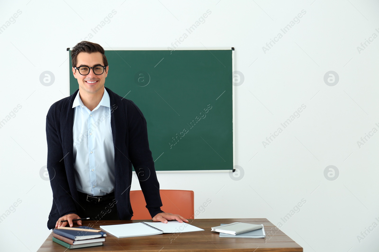 Photo of Young teacher standing near table in classroom