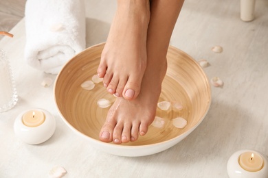 Woman holding her feet over bowl with water and rose petals on floor, closeup. Spa treatment