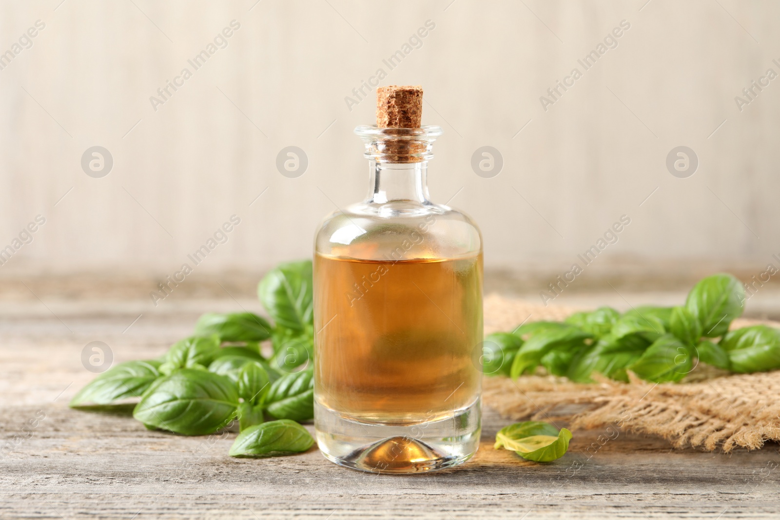 Photo of Glass bottle of basil essential oil and leaves on wooden table