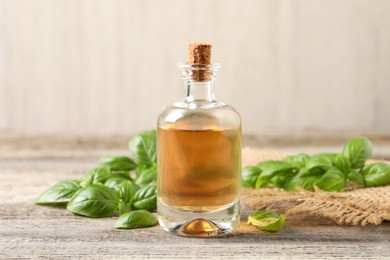 Glass bottle of basil essential oil and leaves on wooden table