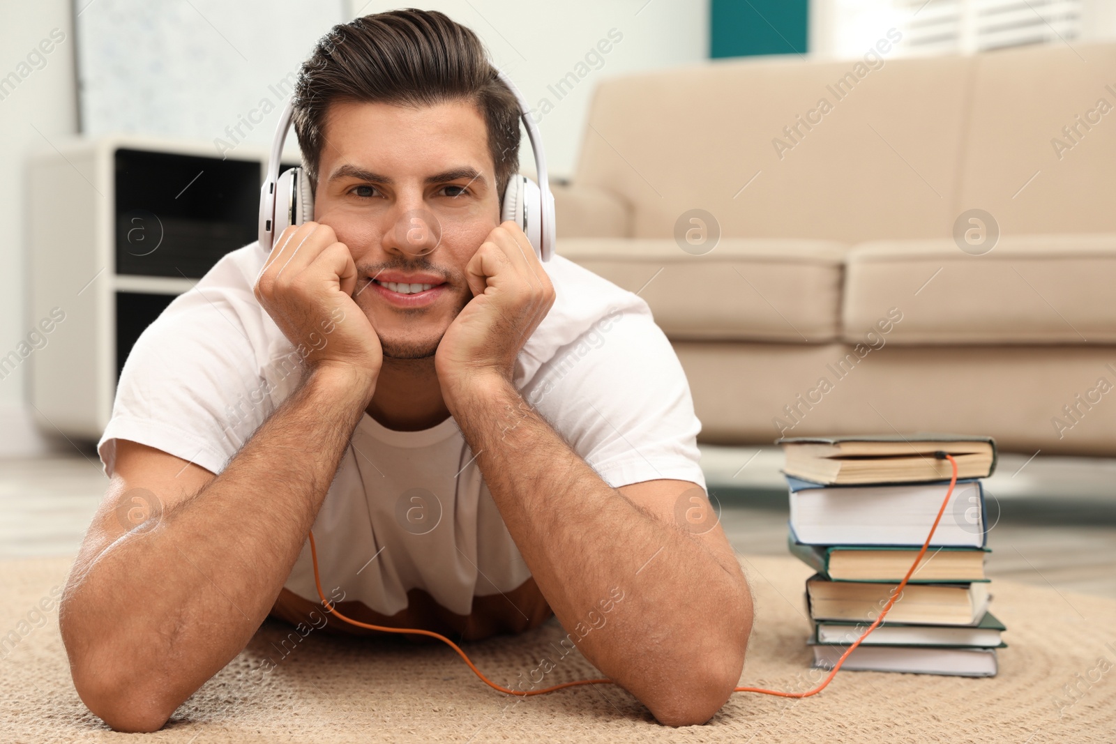 Photo of Man with headphones connected to book
on floor at home. Audiobook concept