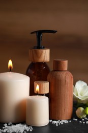 Beautiful spa composition with different care products and burning candles on black table