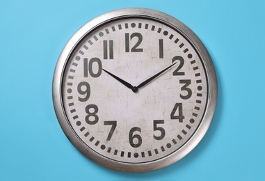 Stylish analog clock hanging on light blue wall