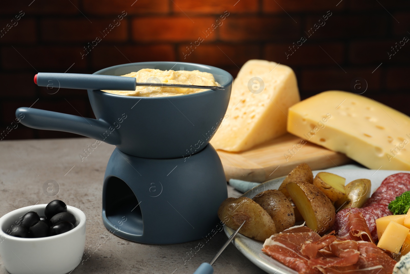 Photo of Tasty melted cheese in fondue pot, fork and snacks on grey table, closeup