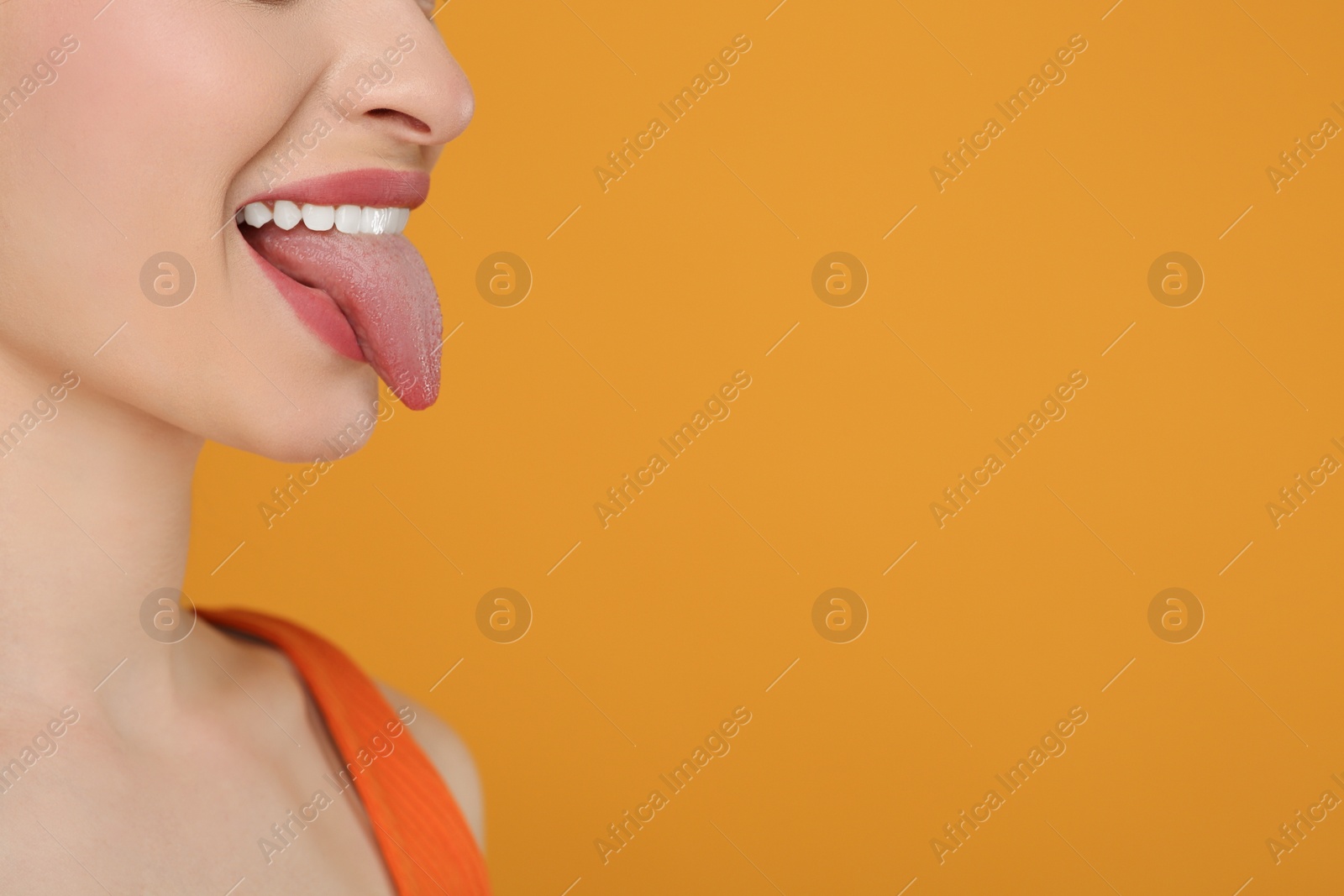 Photo of Happy woman showing her tongue on orange background, closeup. Space for text