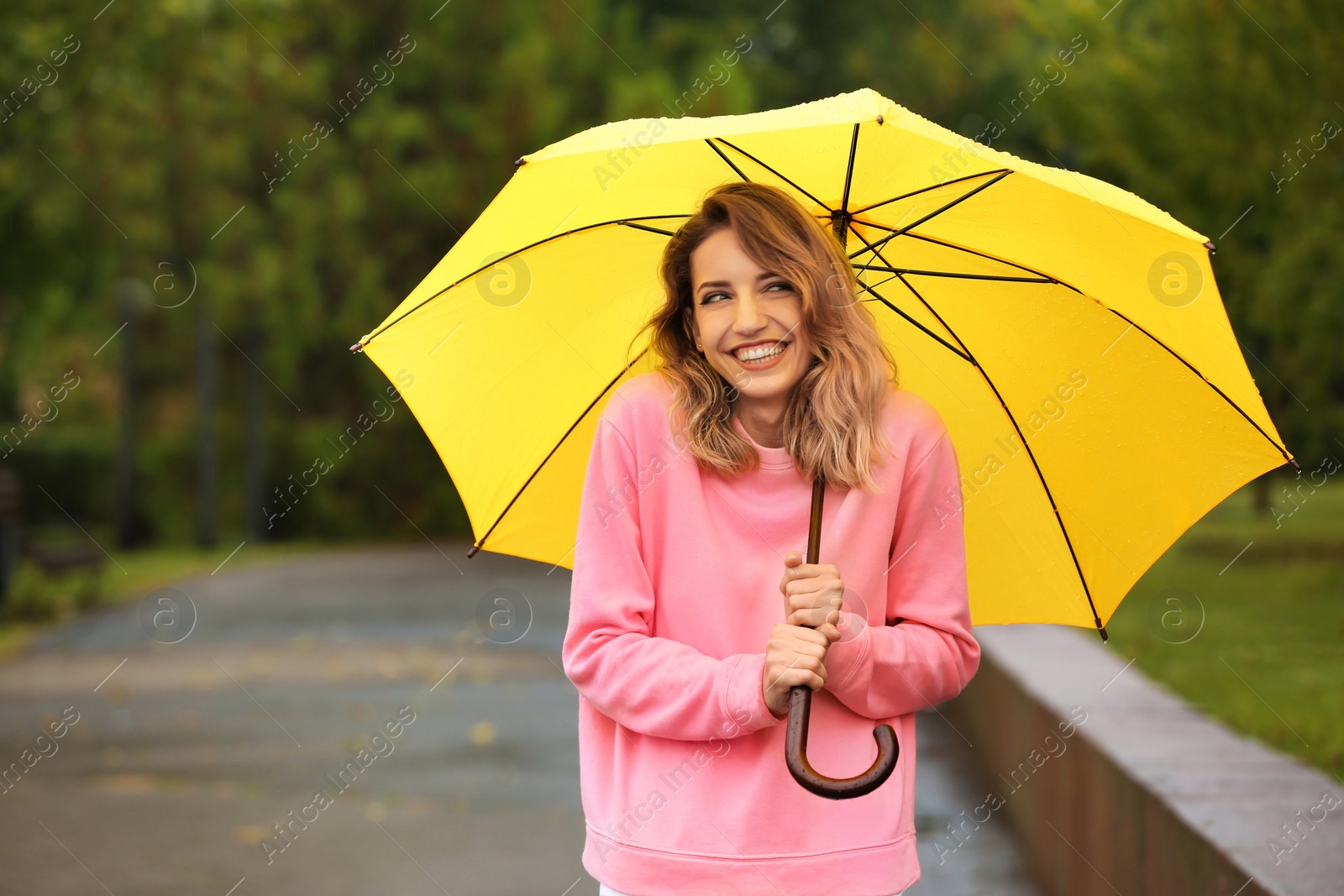 Photo of Happy young woman with bright umbrella under rain outdoors