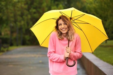 Photo of Happy young woman with bright umbrella under rain outdoors