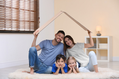 Photo of Happy family sitting under cardboard roof at home. Insurance concept