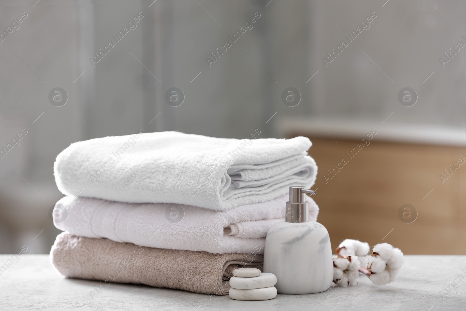 Photo of Clean towels, spa stones and soap dispenser on table in bathroom