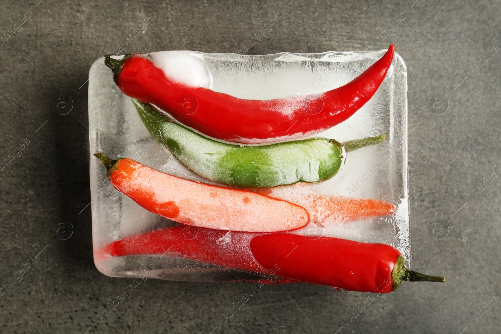 Photo of Chili peppers in ice cube on gray background, top view. Frozen vegetables