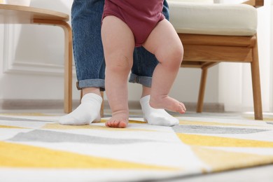 Photo of Mother supporting her baby son while he learning to walk on carpet at home, closeup