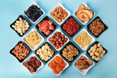 Bowls with dried fruits and nuts on light blue background, flat lay