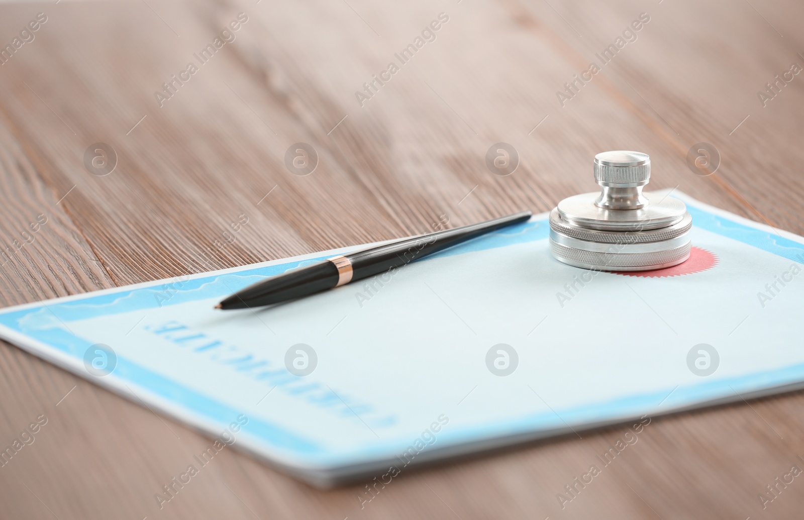 Photo of Certificate form, notary stamp and pen on wooden table