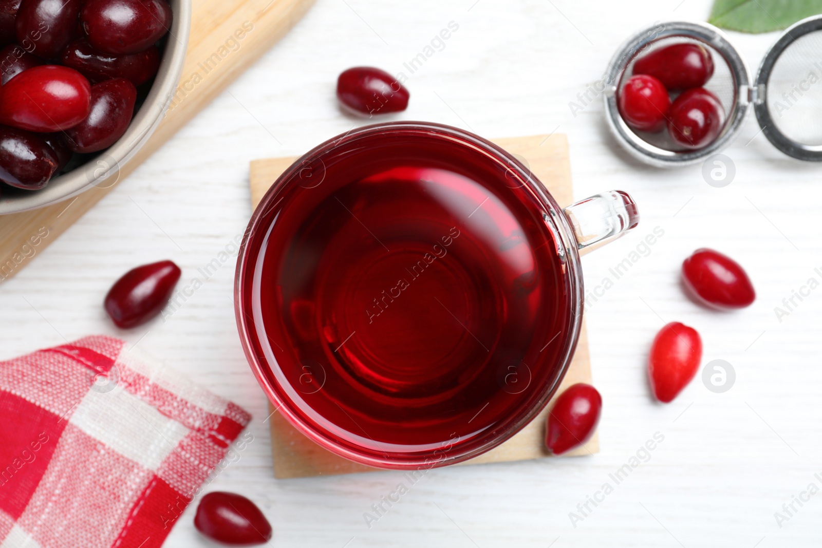 Photo of Glass cup of fresh dogwood tea and berries on white wooden table, flat lay