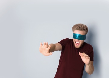 Photo of Young man wearing blue blindfold on light background