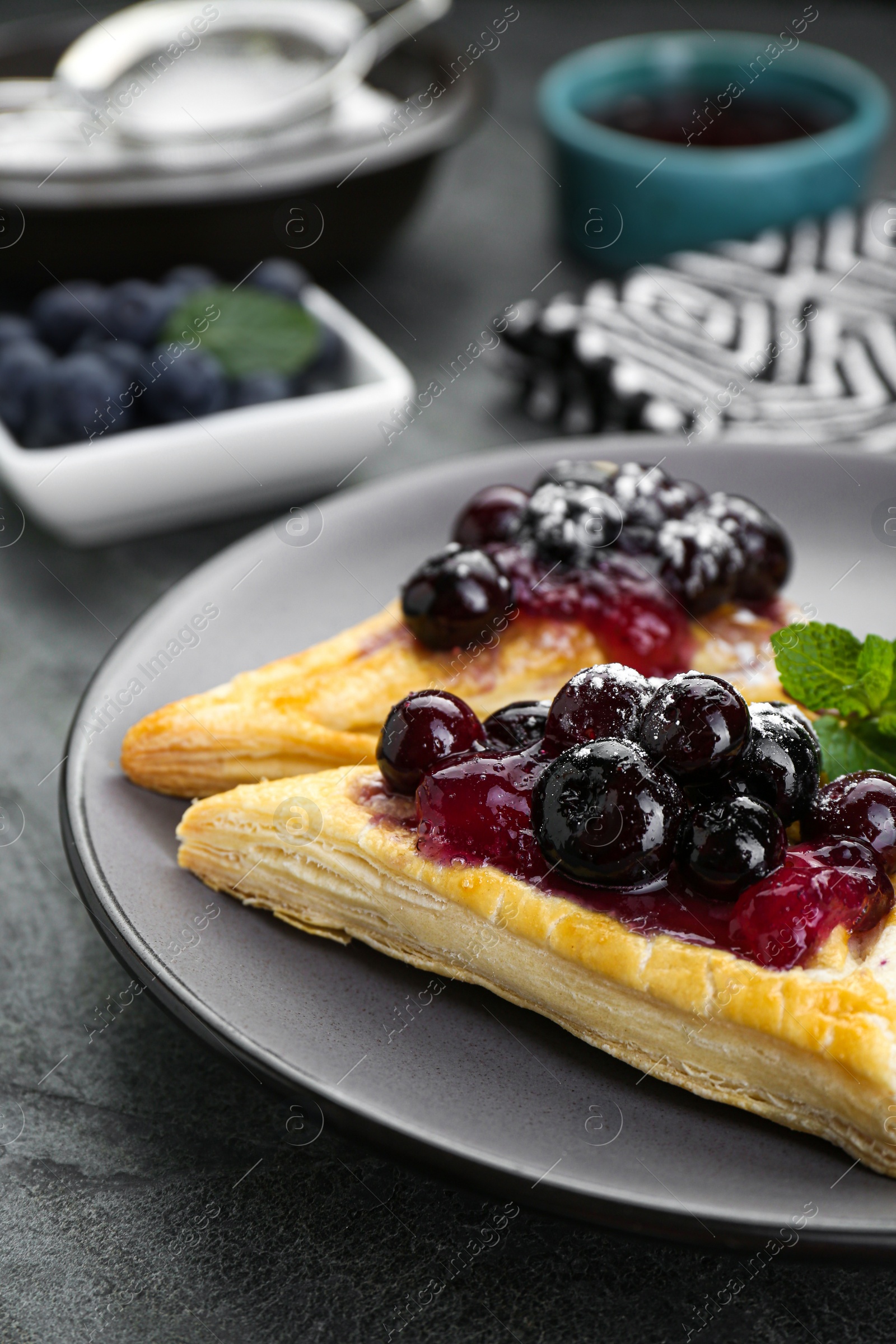 Photo of Fresh tasty puff pastry with sugar powder, jam, sweet berries and mint on grey table, closeup