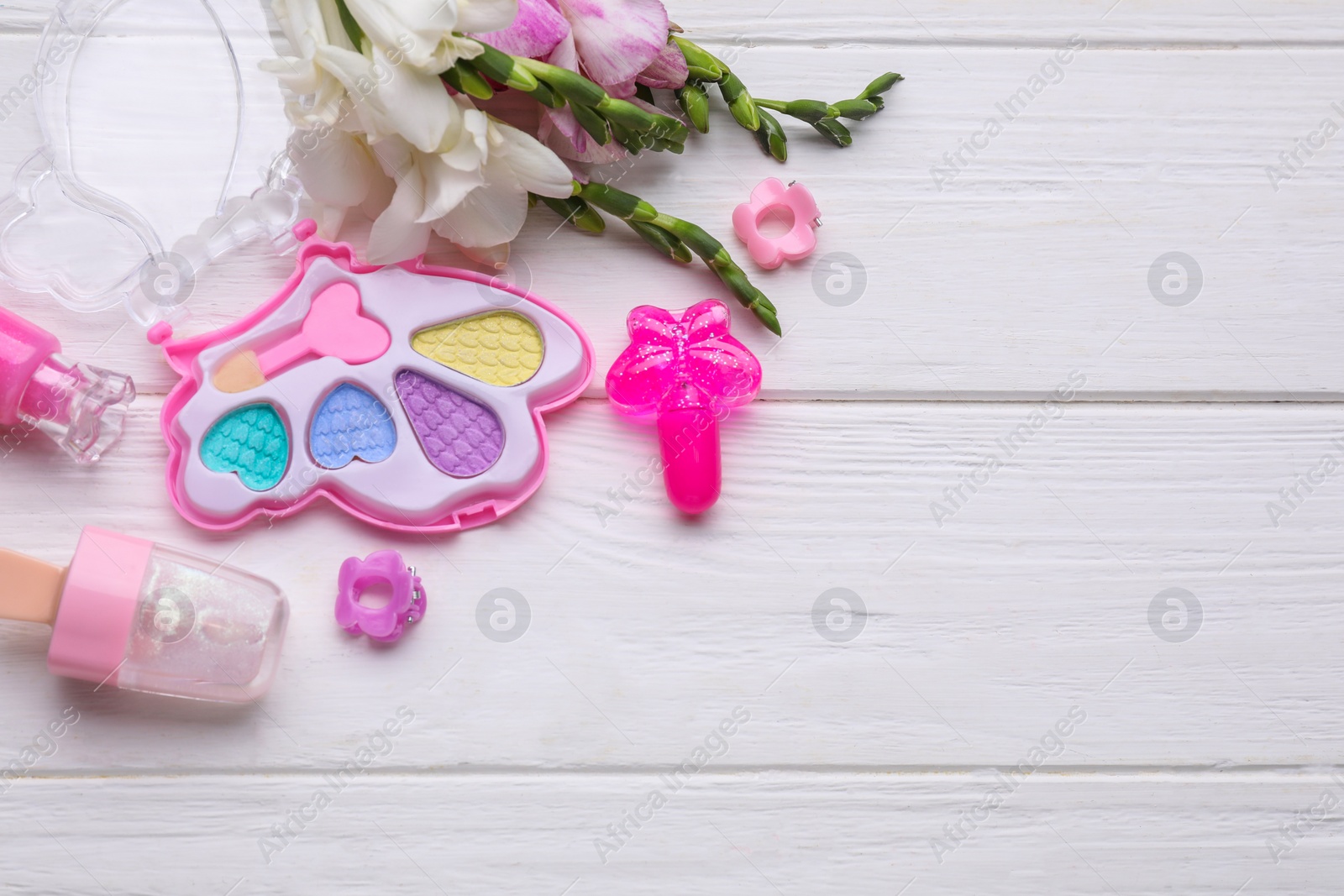 Photo of Decorative cosmetics for kids. Eye shadow palette, lipsticks, accessories and flowers on white wooden table, flat lay. Space for text