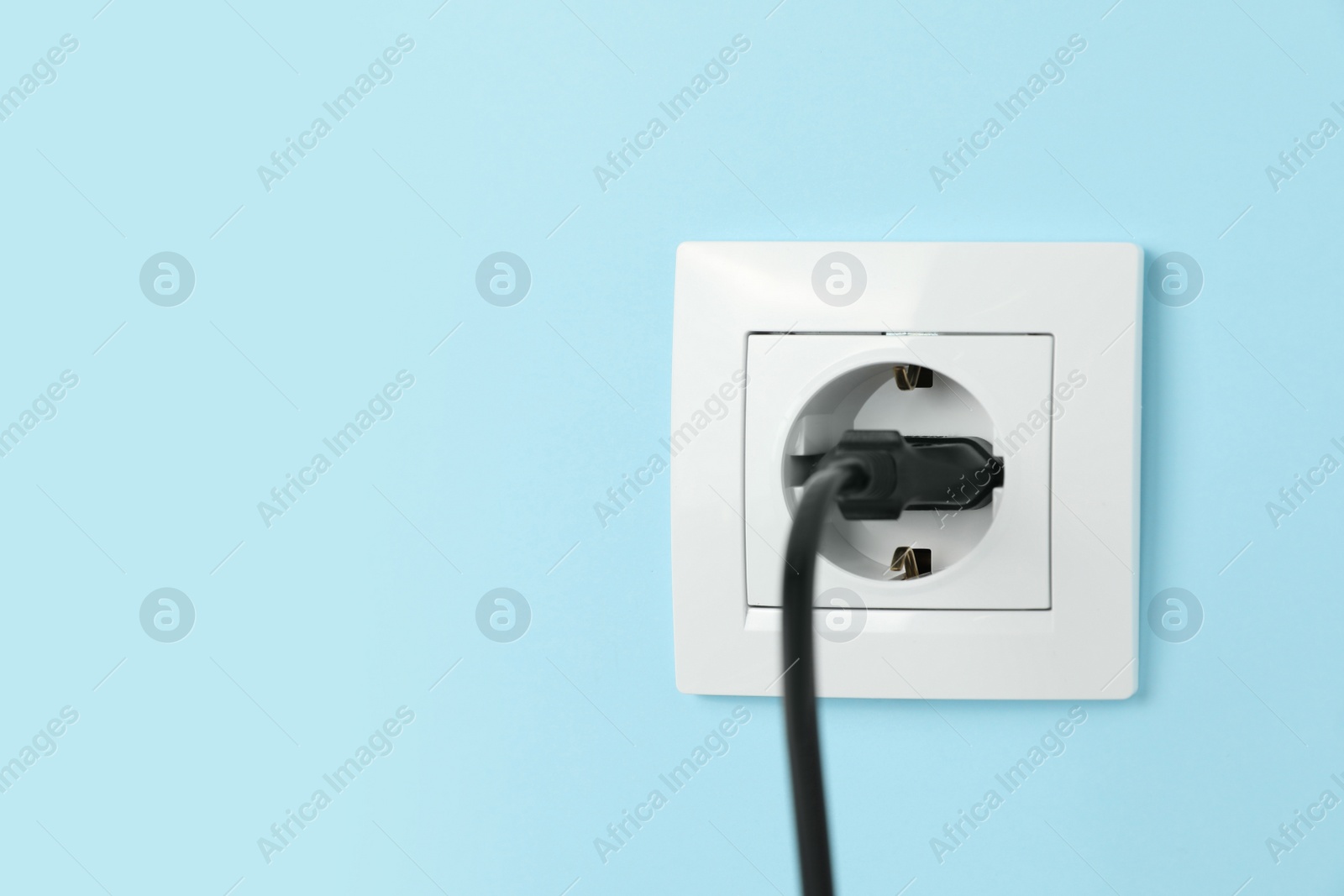 Photo of Power socket with inserted plug on light blue wall, space for text. Electrical supply