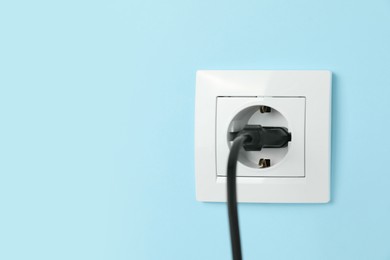 Power socket with inserted plug on light blue wall, space for text. Electrical supply
