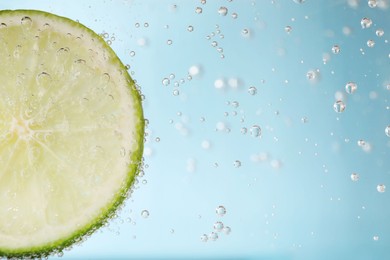 Juicy lime slice in soda water against light blue background, closeup. Space for text