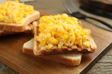 Photo of Delicious breakfast with scrambled eggs and toasted bread served on wooden board, closeup