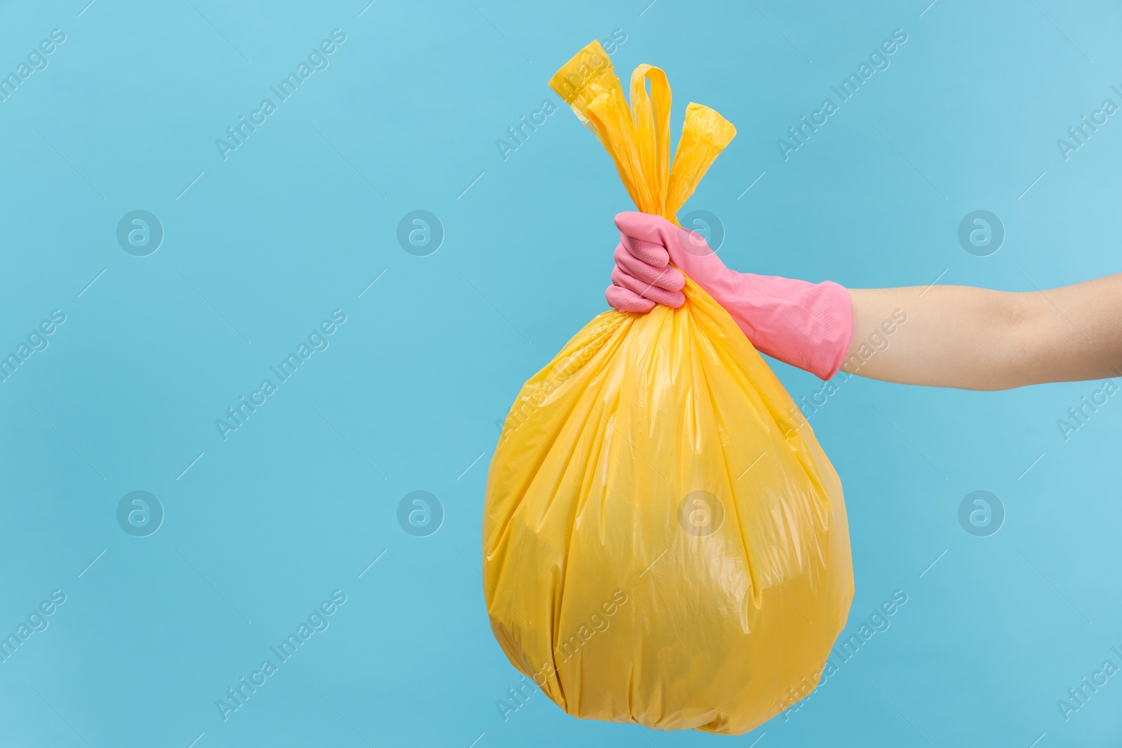 Photo of Woman holding plastic bag full of garbage on light blue background, closeup. Space for text