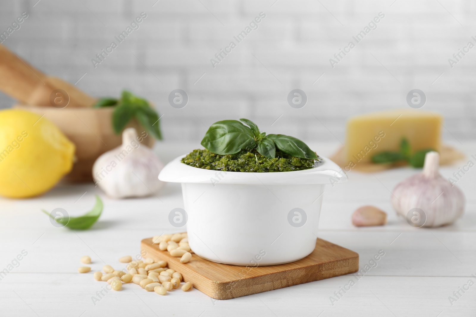 Photo of Delicious pesto sauce in bowl and ingredients on white wooden table