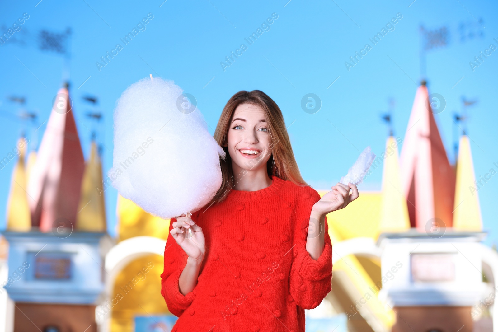 Photo of Young cheerful woman having fun with  cotton candy in amusement park