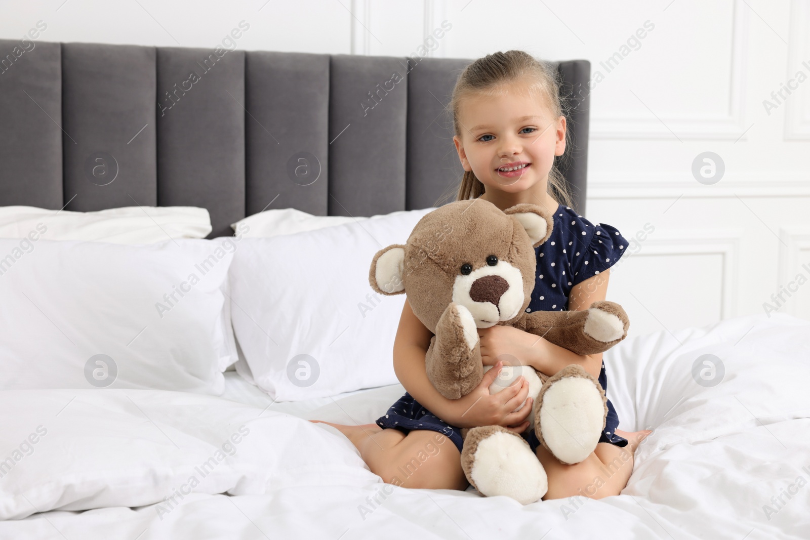 Photo of Cute little girl with teddy bear on bed. Space for text