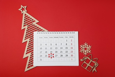 Calendar with marked Boxing Day date and Christmas decorations on red background, flat lay