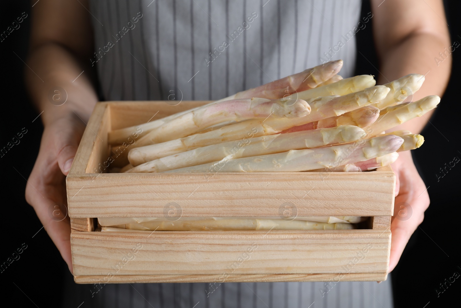 Photo of Woman holding wooden crate with fresh white asparagus on black background, closeup