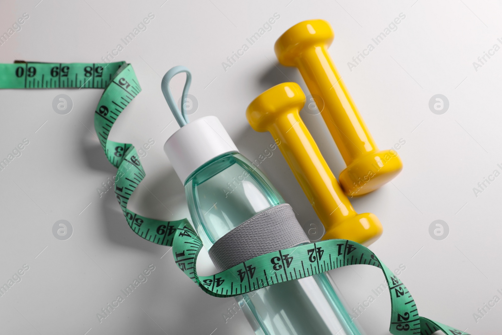 Photo of Measuring tape, dumbbells and bottle with water on white background, flat lay. Weight control concept