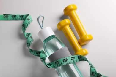 Measuring tape, dumbbells and bottle with water on white background, flat lay. Weight control concept