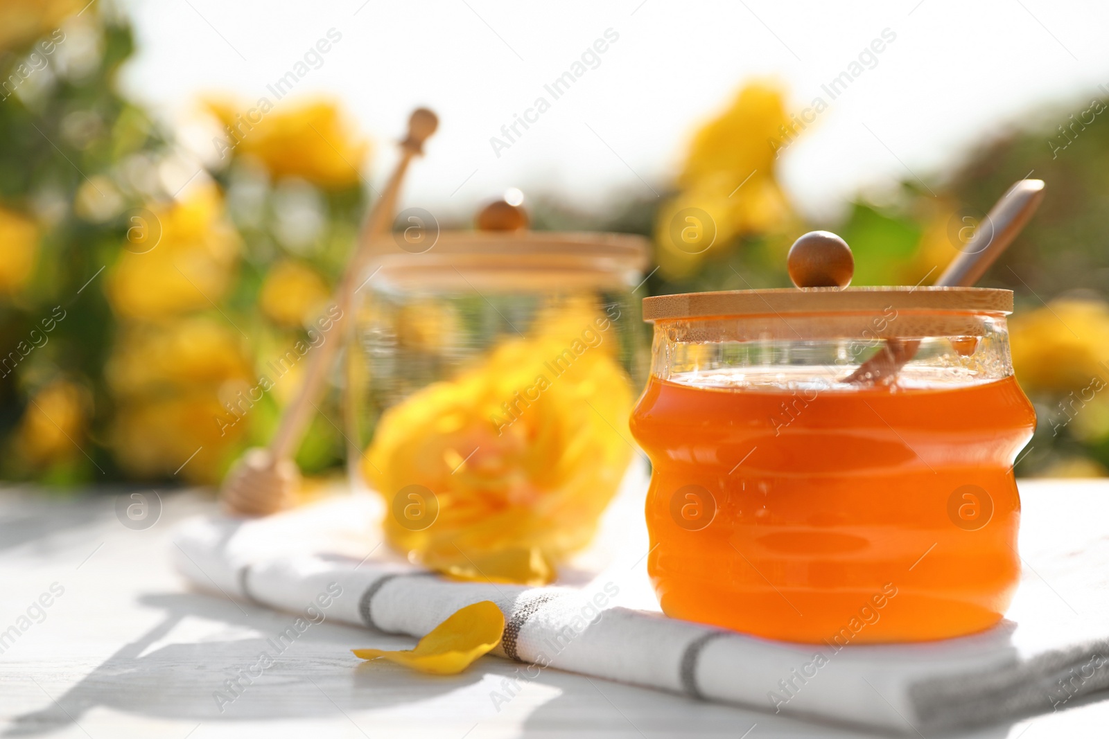 Photo of Jar with fresh rose honey on white wooden table outdoors. Space for text