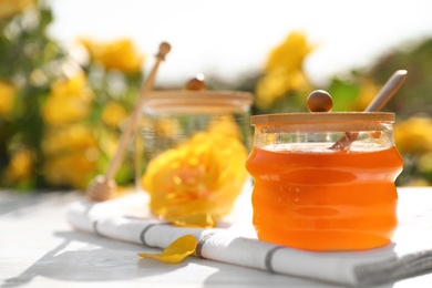 Photo of Jar with fresh rose honey on white wooden table outdoors. Space for text