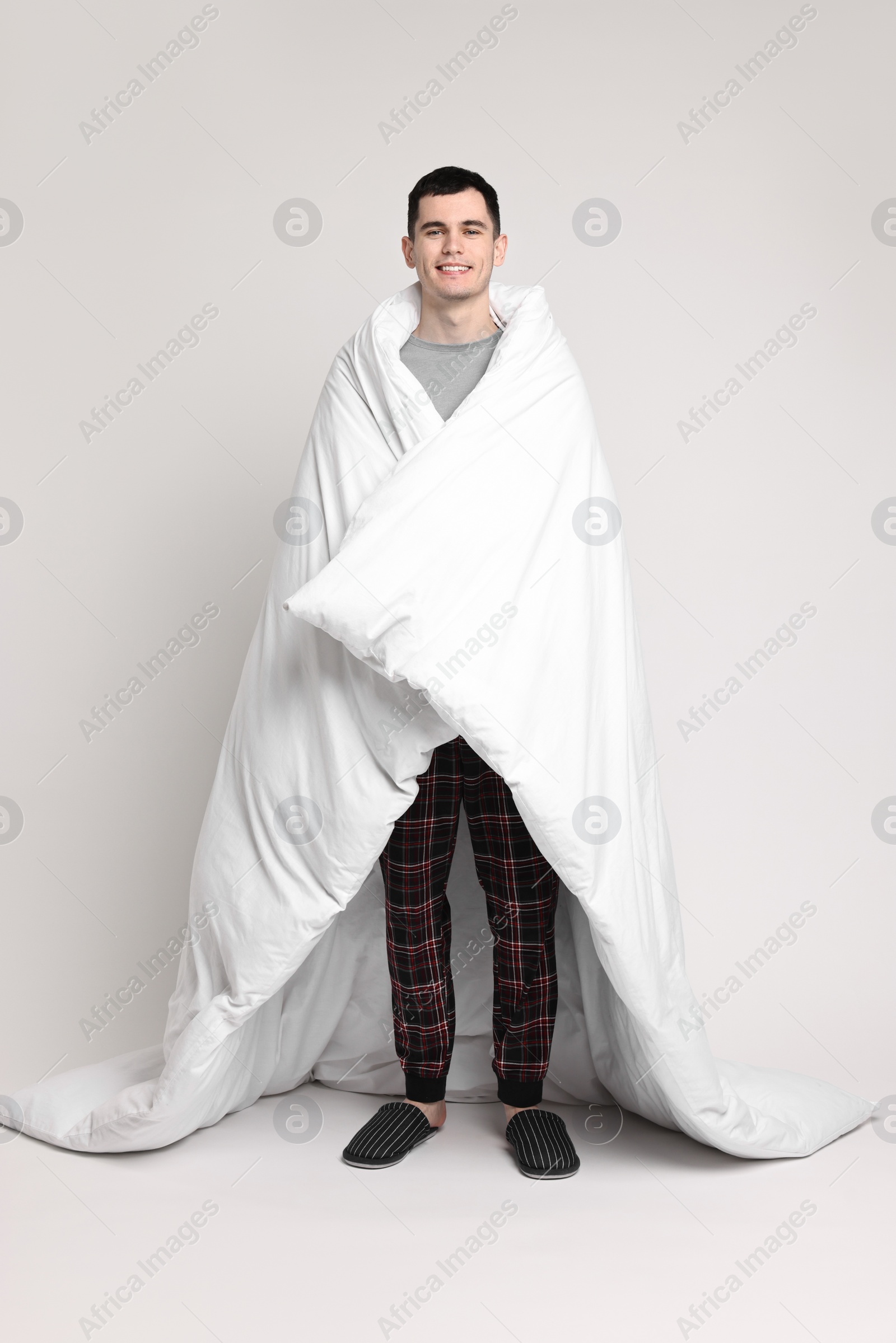 Photo of Happy man in pyjama wrapped in blanket on light grey background