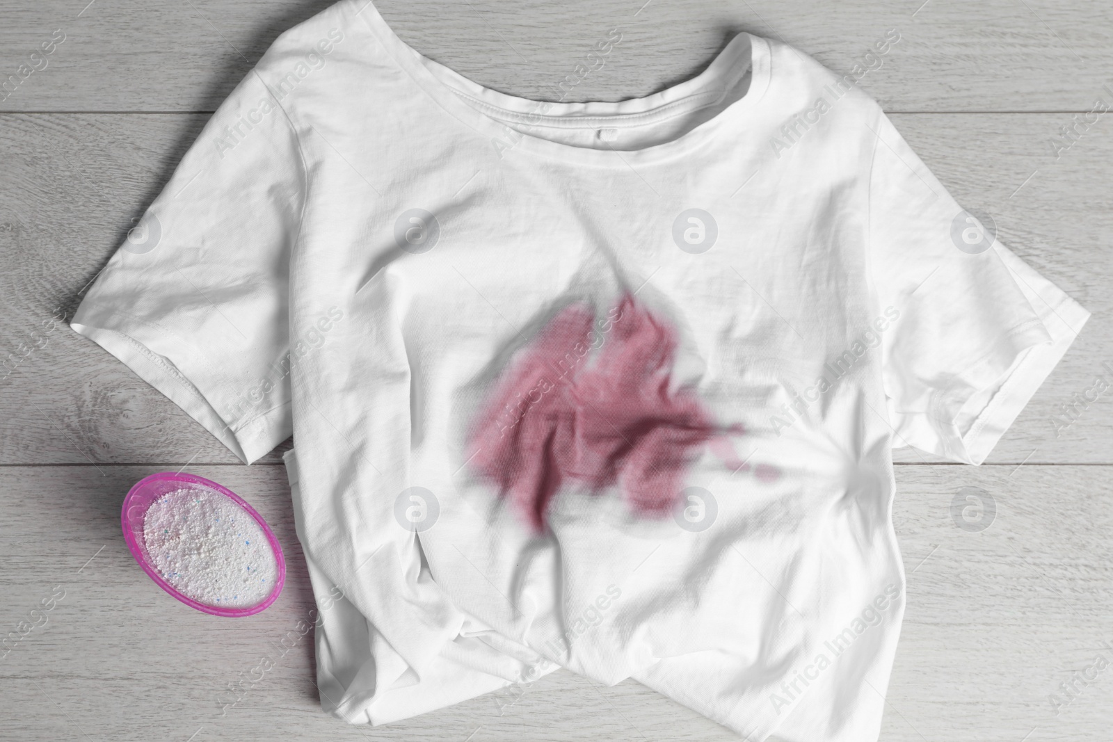 Photo of White t-shirt with stain and powdered detergent on wooden surface, flat lay. Hand washing laundry