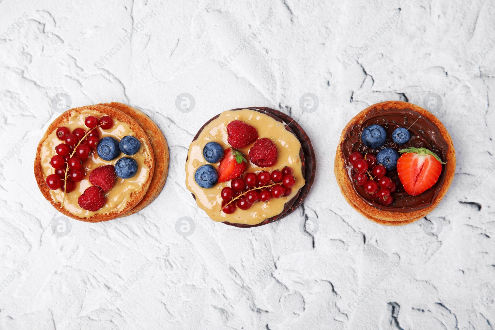 Photo of Tasty organic rusks and crunchy rice cakes with different toppings on white textured table, flat lay