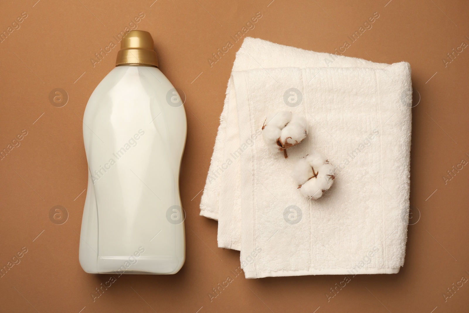 Bottle of fabric softener, terry towel and beautiful cotton flowers on brown background, flat lay Photo of Bottle of fabric softener, terry towel and beautiful cotton flowers on brown background, flat lay