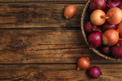 Photo of Onion bulbs in basket on wooden table, top view. Space for text