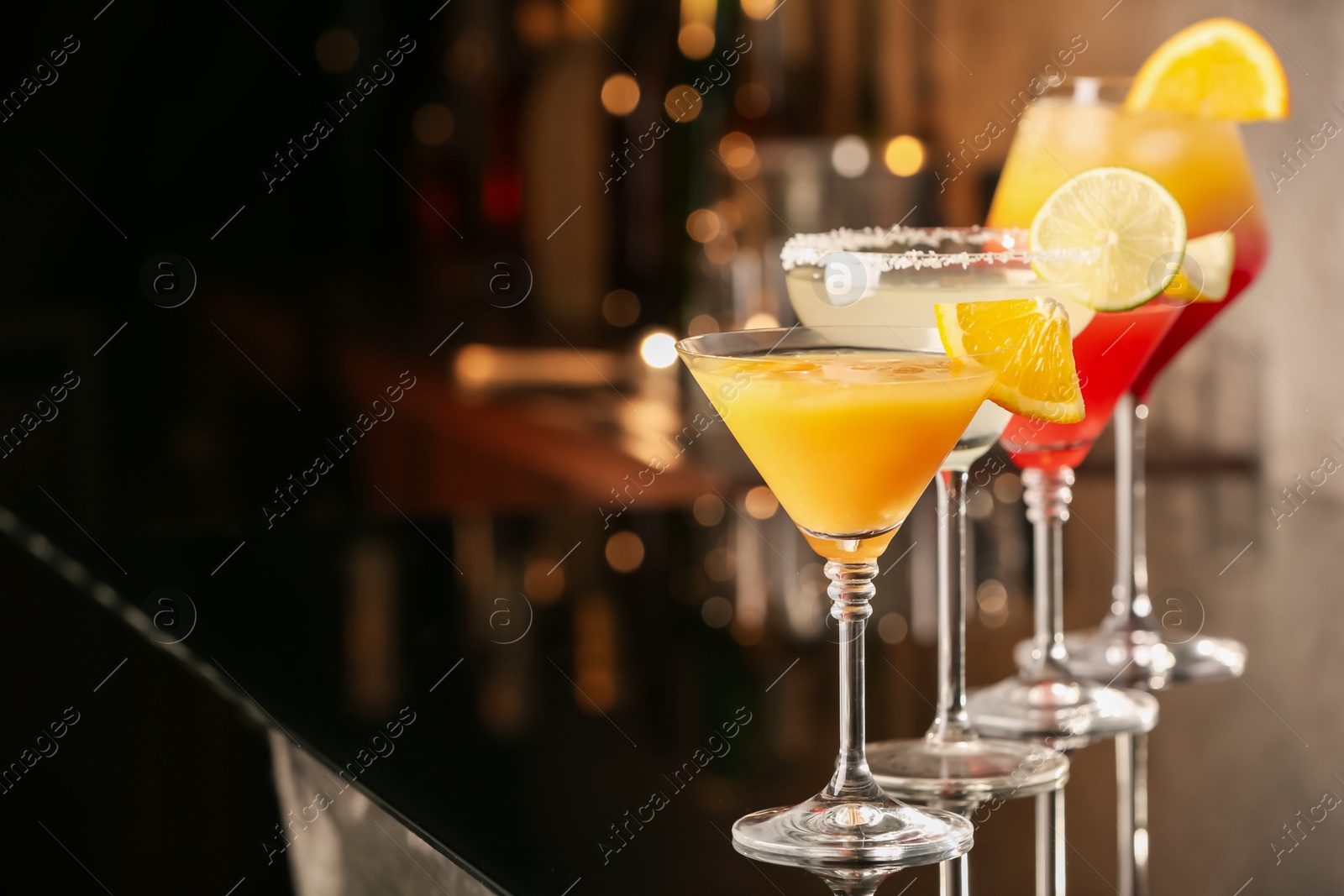 Photo of Different delicious cocktails on black table in bar. Space for text