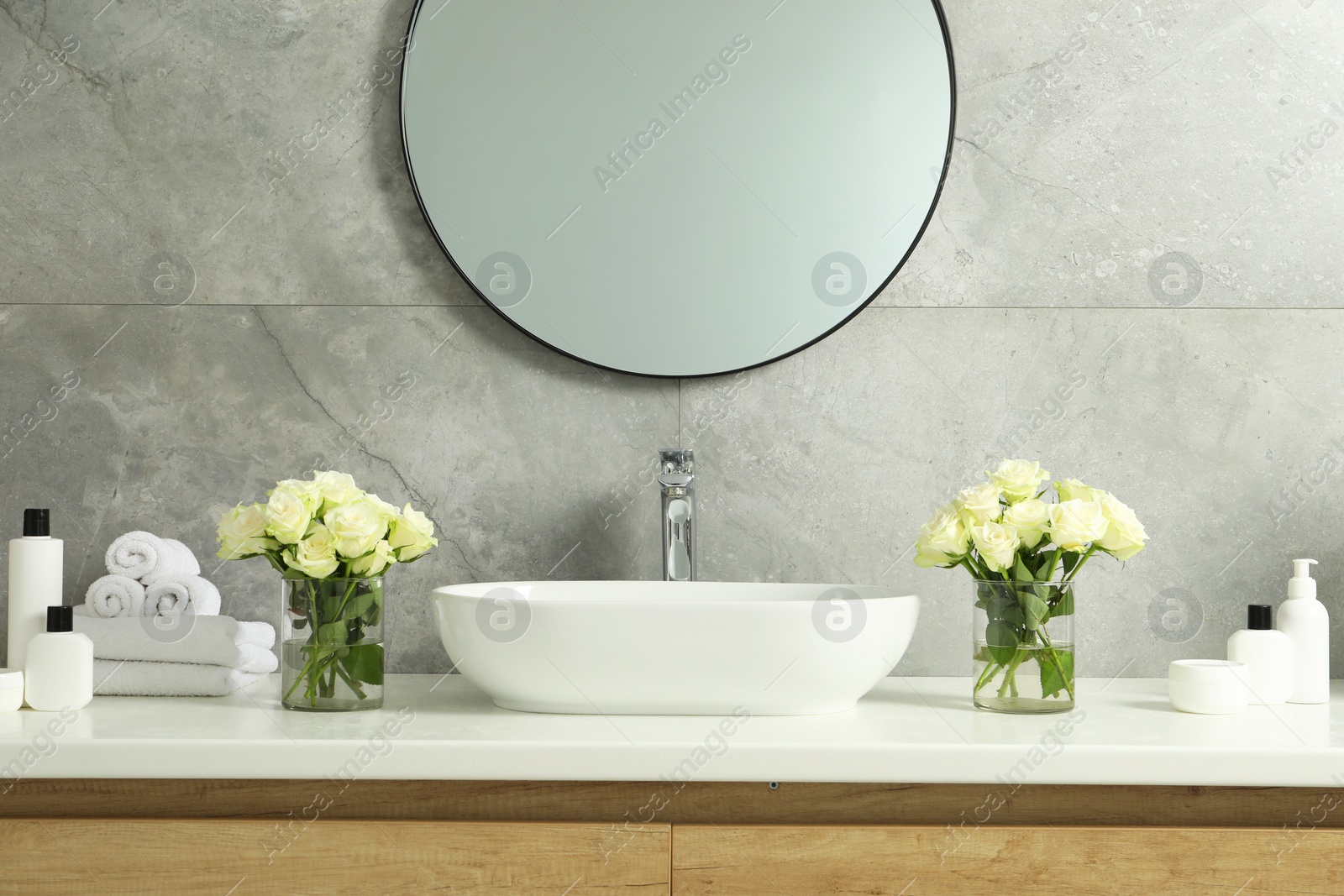 Photo of Beautiful roses, bath accessories, sink and mirror in bathroom